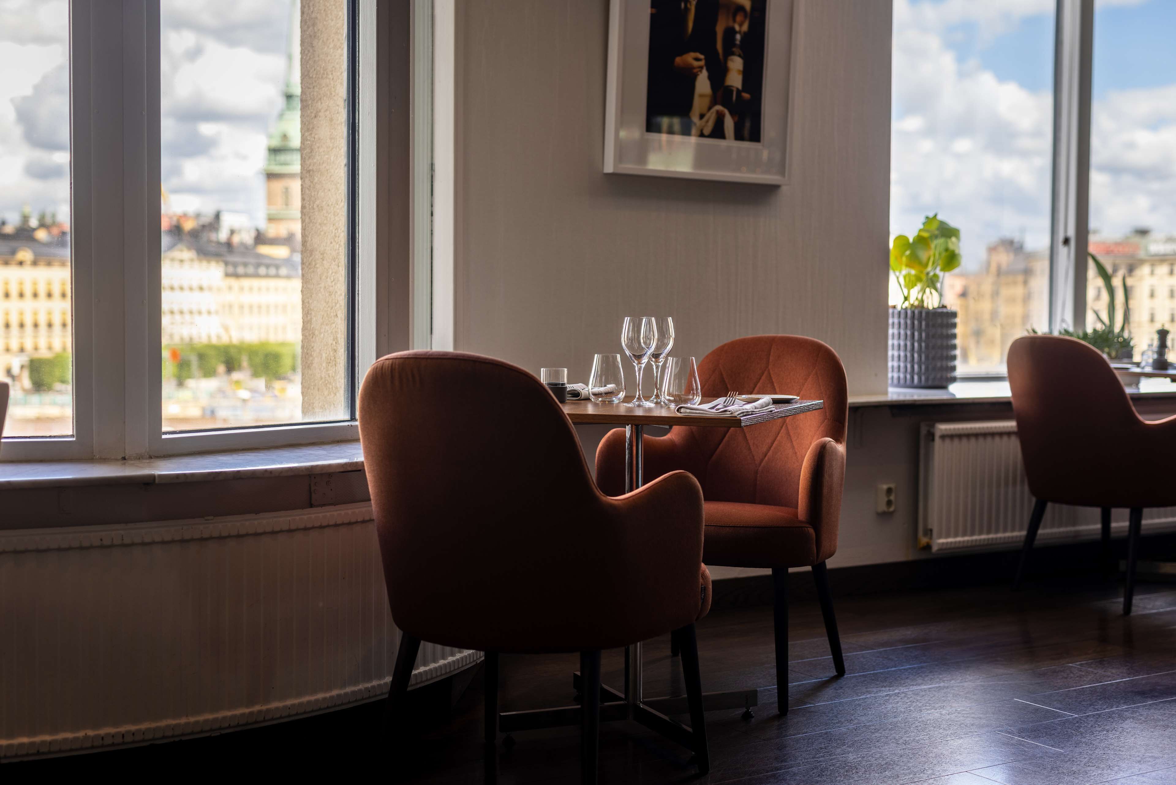 A dining area with a table set for two, large windows with a city view, and a framed picture on the wall.