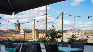 An outdoor seating area with wicker chairs and tables, overlooking a cityscape with historic buildings and a prominent tower. - Hilton Stockholm Slussen (Stockholm)