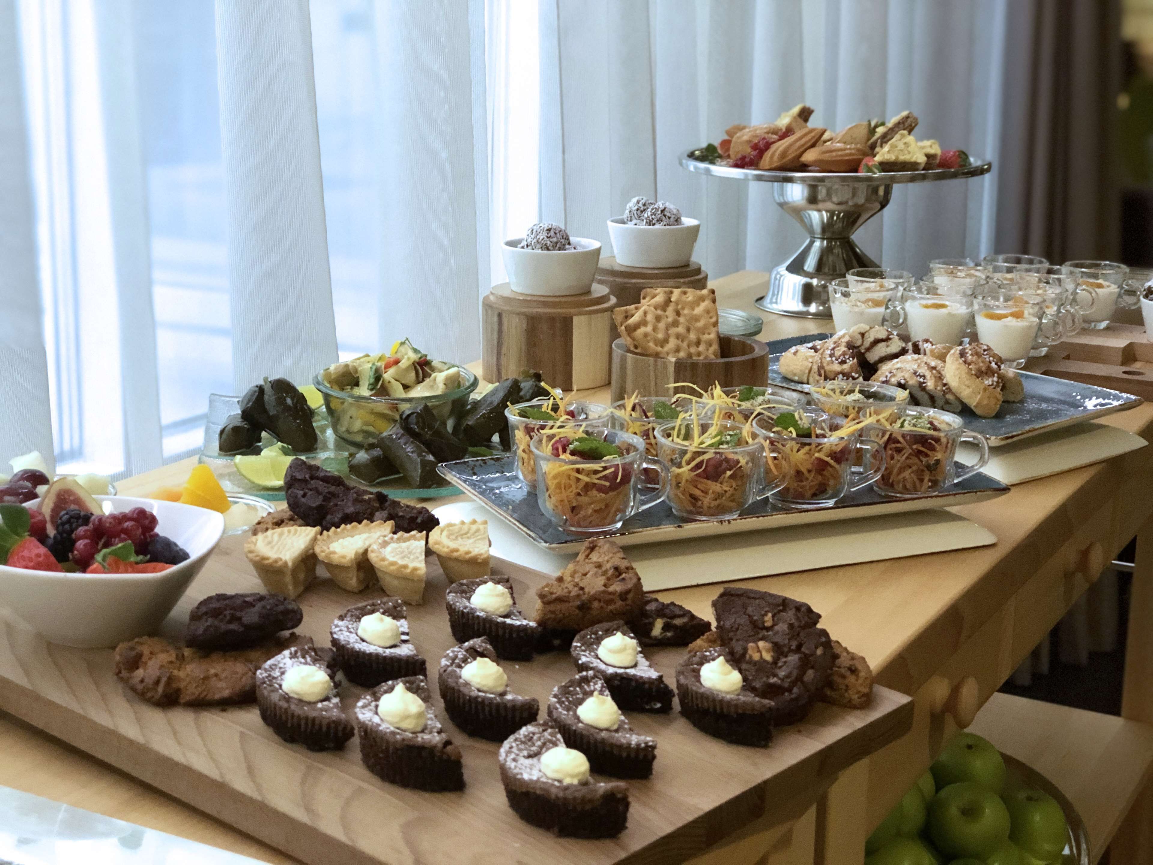 Una mesa de bufé con diversos alimentos, incluyendo pasteles, ensaladas y bebidas.