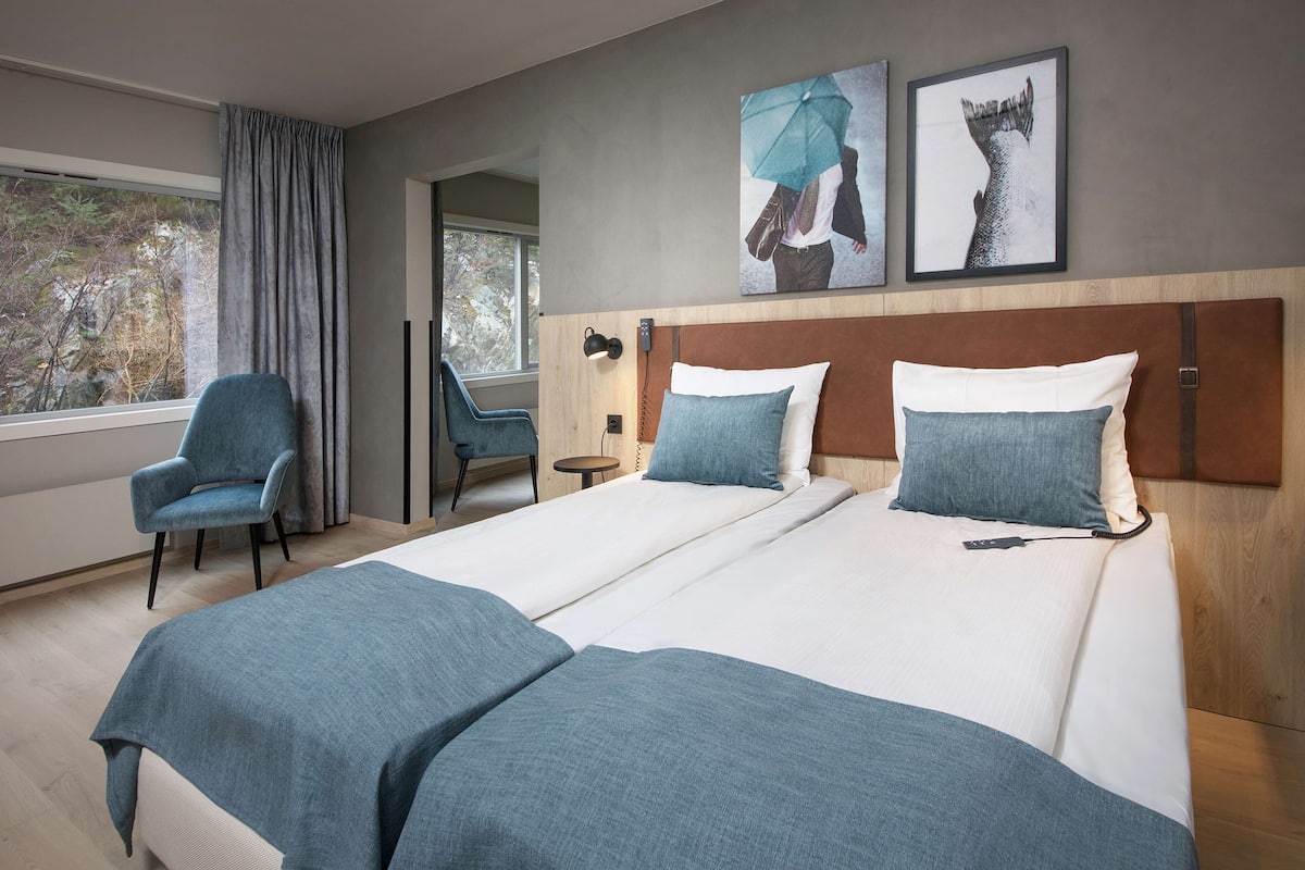 Habitación de hotel con dos camas, una silla, un escritorio y obras de arte en la pared.