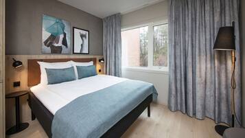 A modern bedroom with a large bed, a bedside table, a lamp, and a window with curtains.