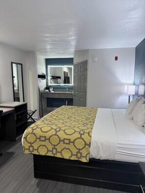 A hotel room with a bed, a desk, a mirror, a bathroom with a sink and mirror, and a door.