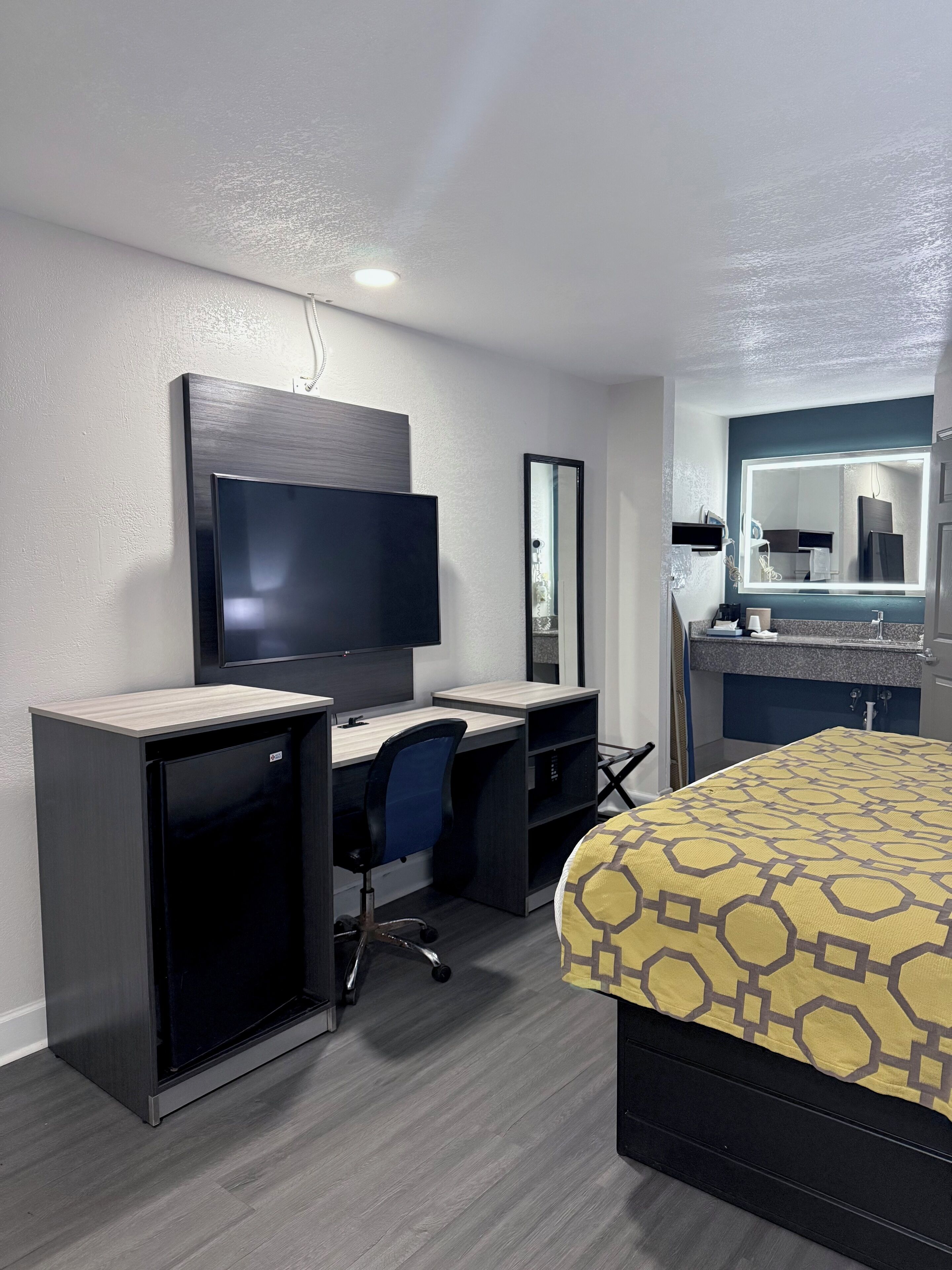 A hotel room with a desk, chair, television, bed, and a large mirror.