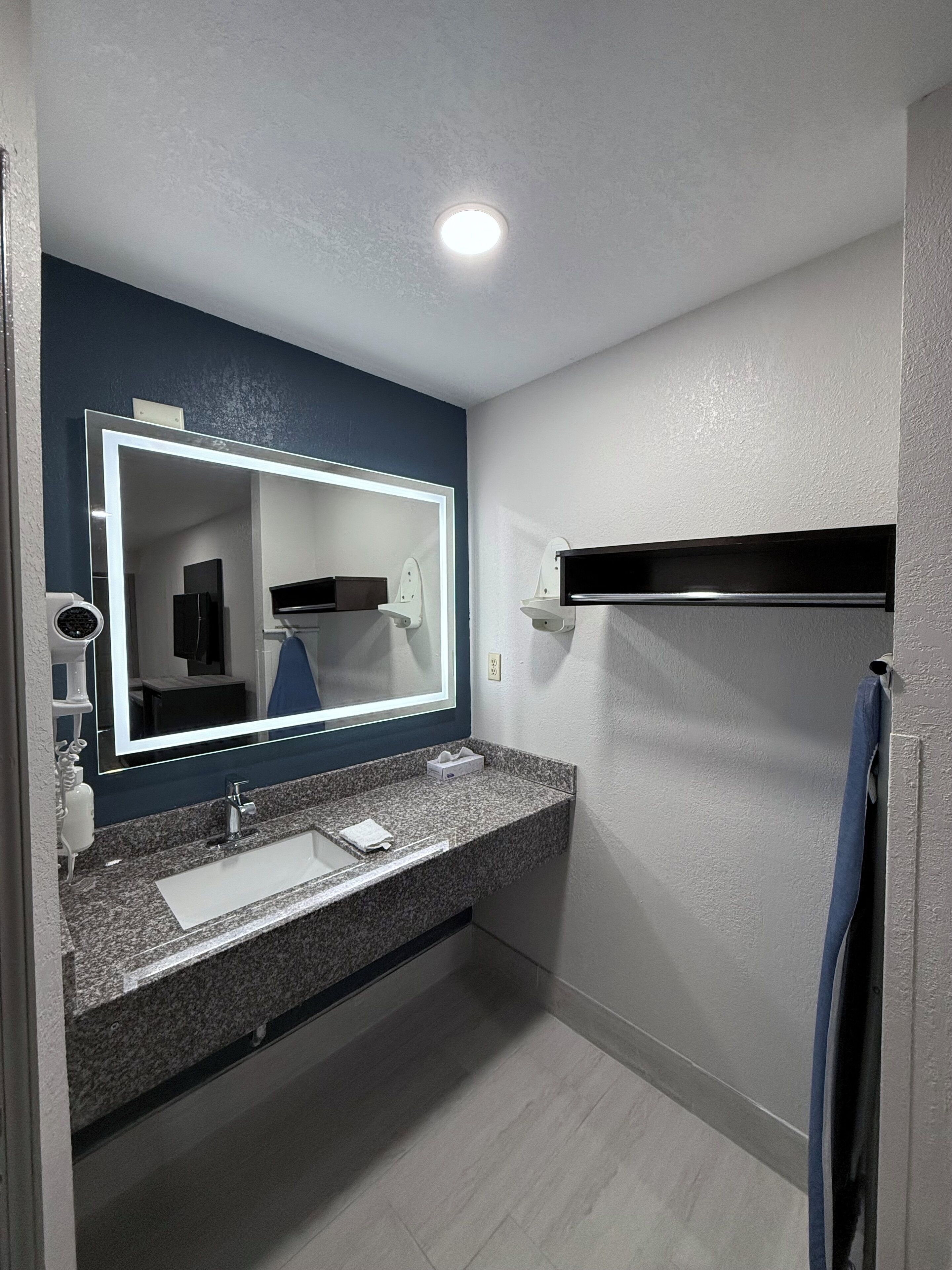 A modern bathroom with a granite countertop, a white sink, a large mirror, and a ceiling light.