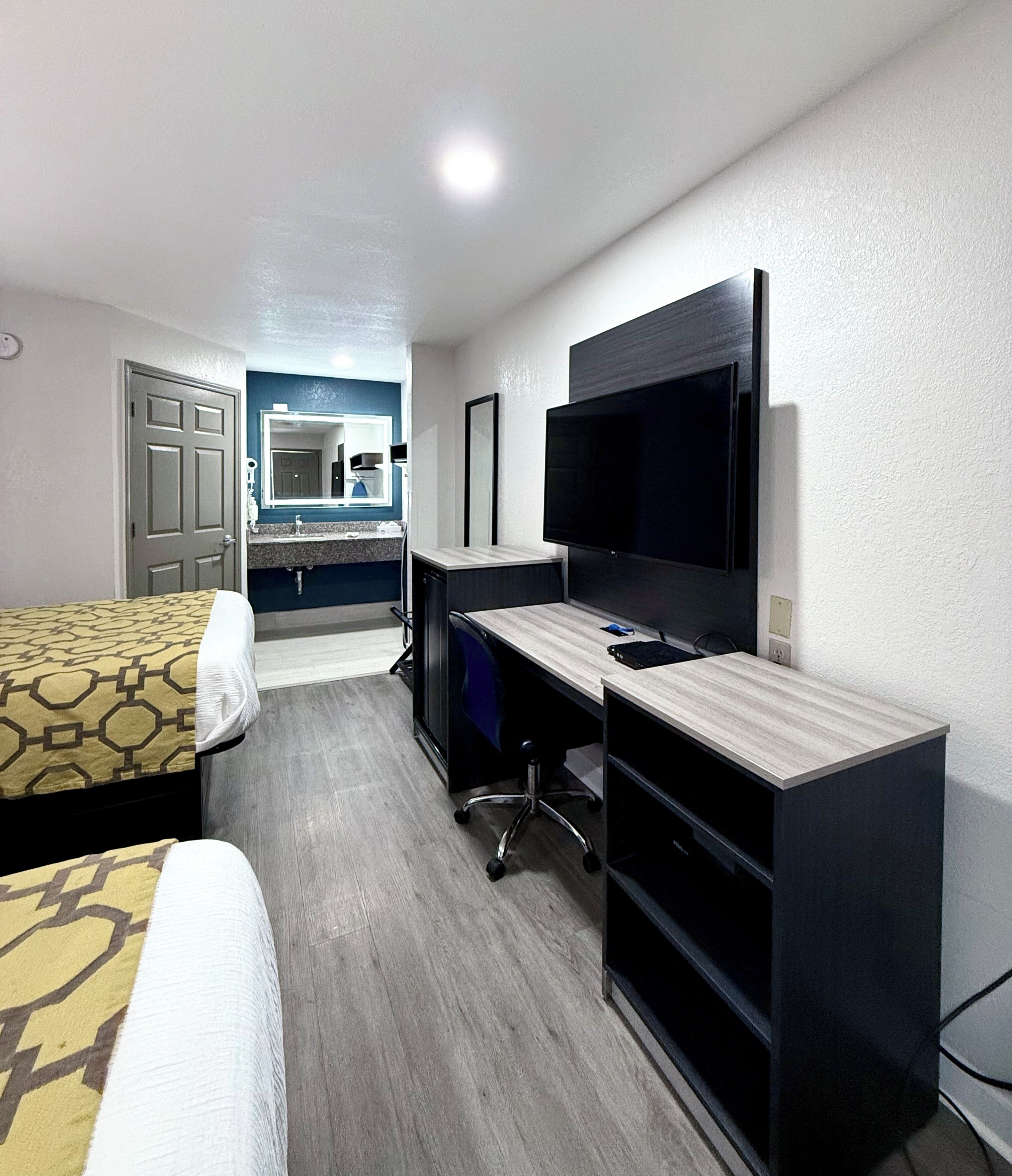 Quarto de hotel com cama, escrivaninha, televisão e banheiro com espelho e pia.