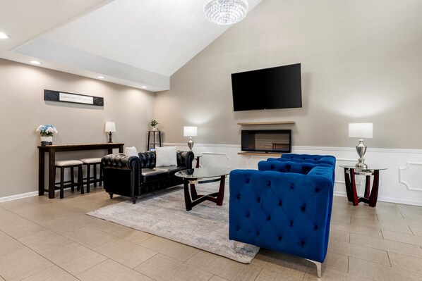 Una sala de estar moderna con un sofá de cuero negro, sillones de terciopelo azul, un televisor de pantalla plana y una chimenea.