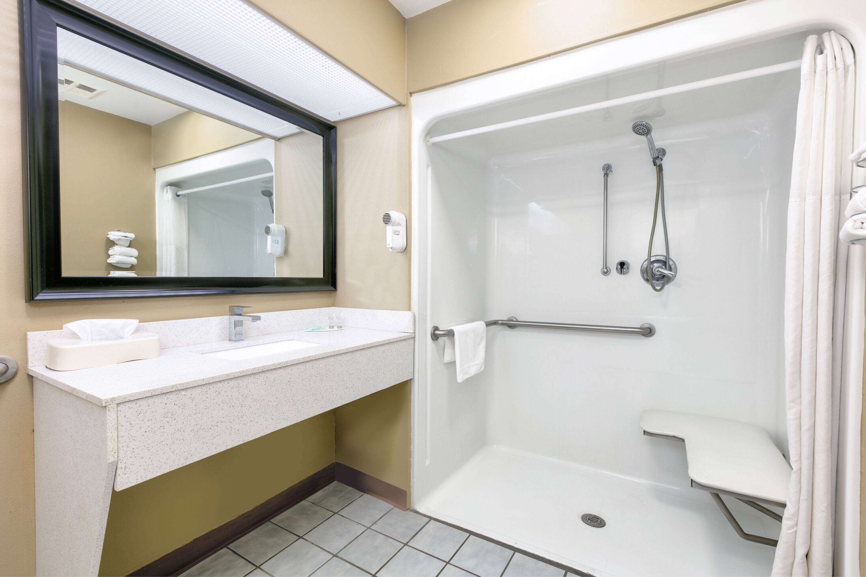A bathroom with a shower, a sink, a mirror, and a towel rack.
