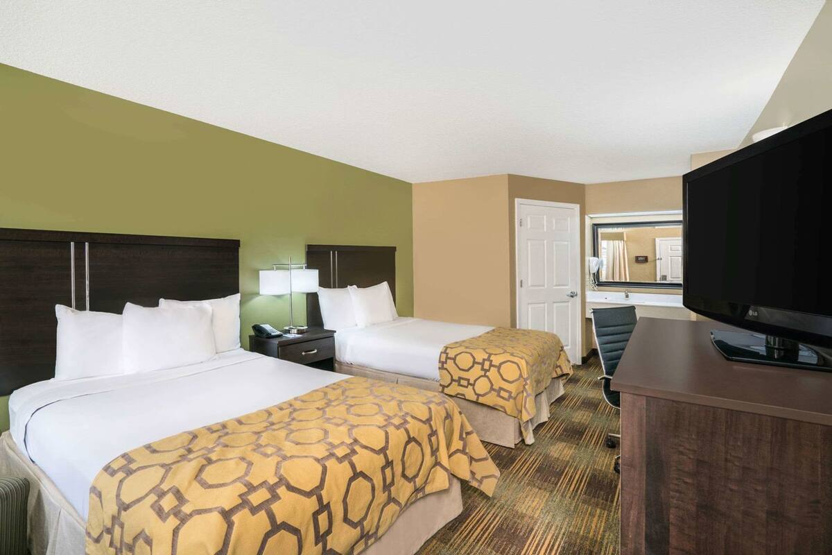 Ein Hotelzimmer mit zwei Betten, einem Fernseher, einem Schreibtisch und einem Fenster.