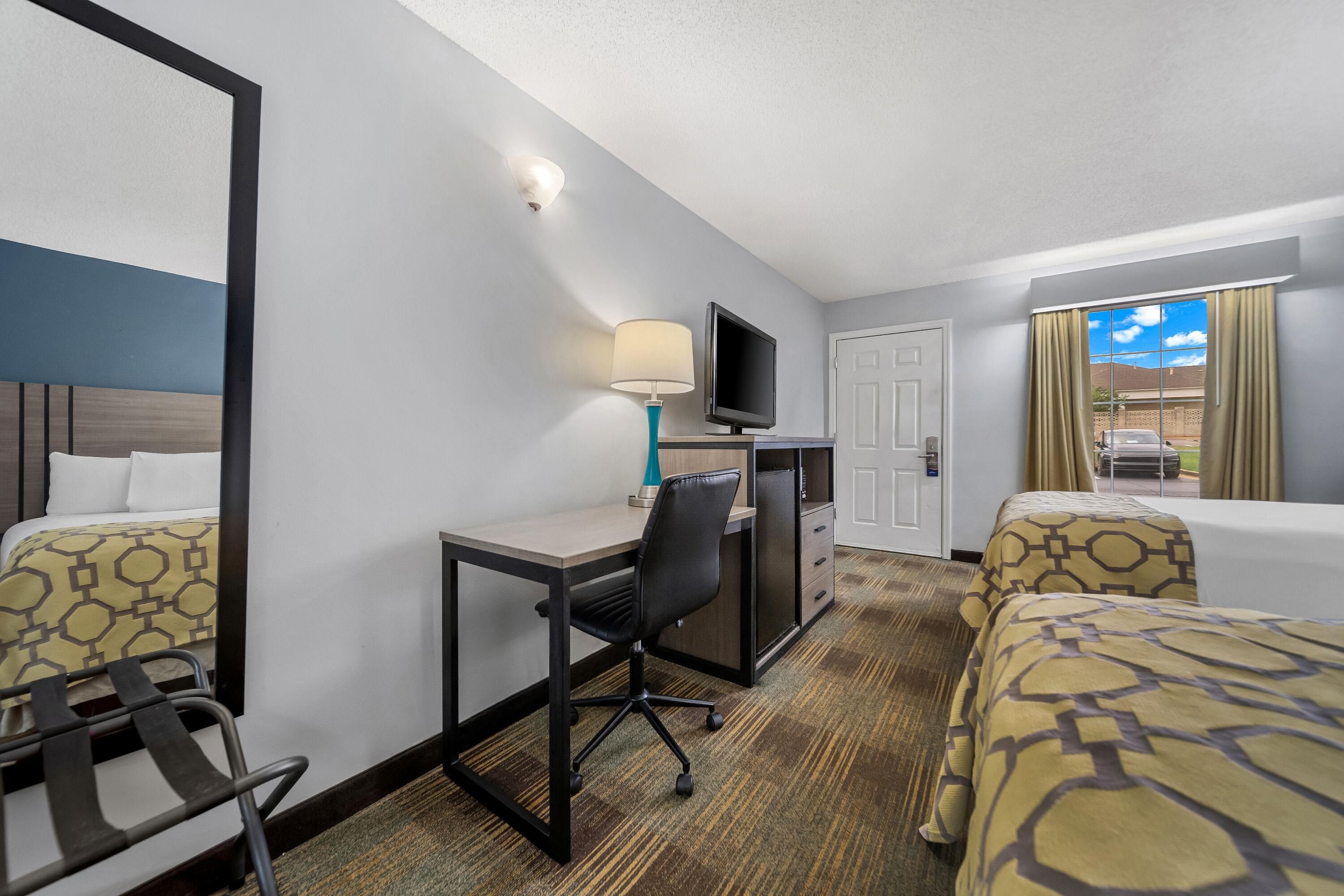 A hotel room with a bed, a desk with a chair, a television, and a window with curtains.