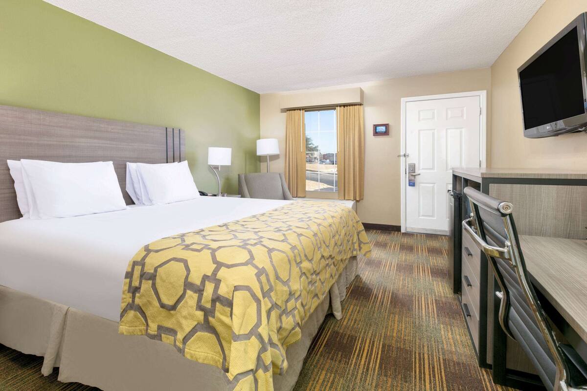 Ein Hotelzimmer mit einem großen Bett, zwei Nachttischlampen, einem an der Wand befestigten Fernseher und einer Tür zum Außenbereich.