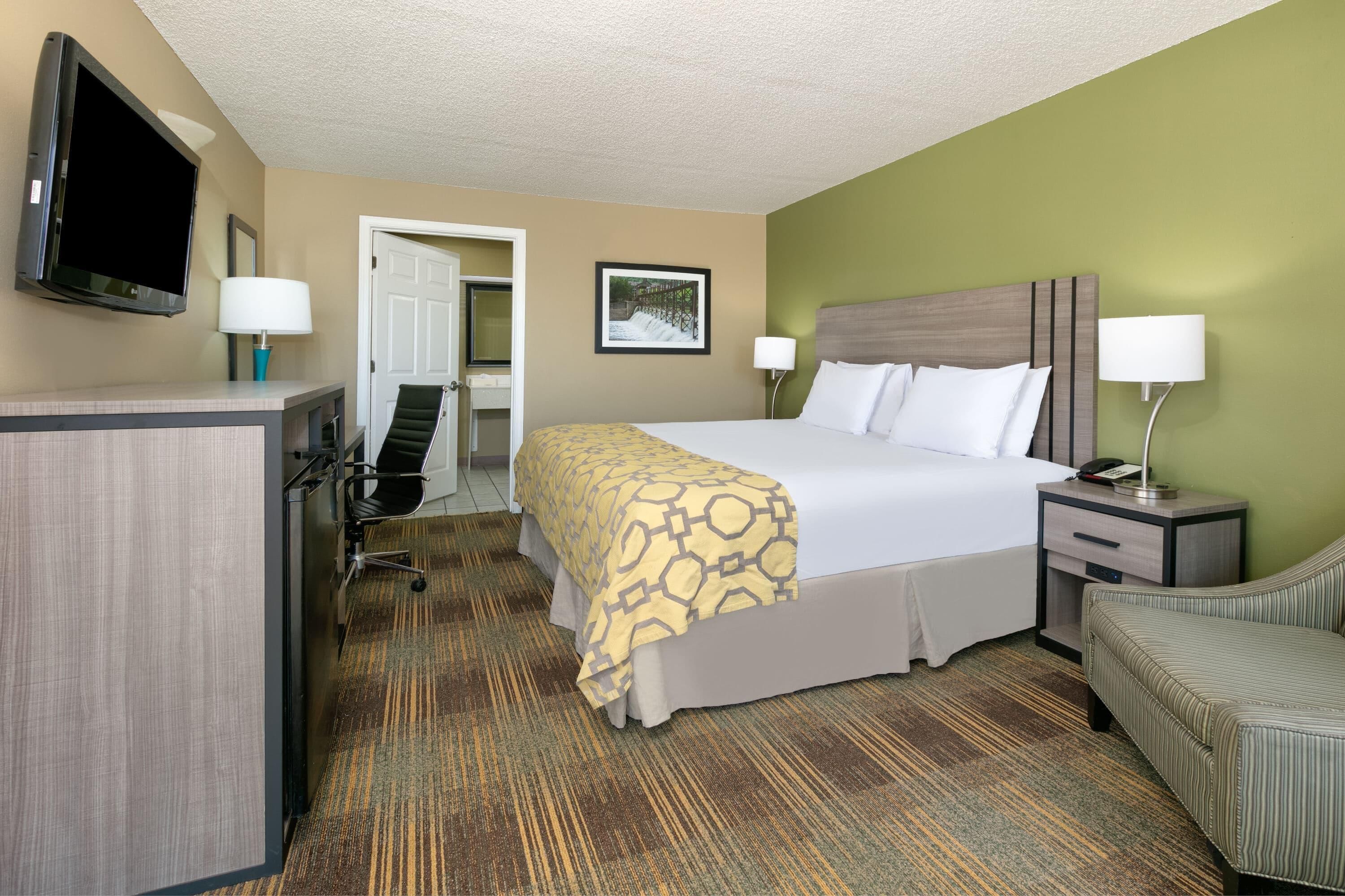 A hotel room with a bed, bedside tables, a desk, a chair, a television, and a door.
