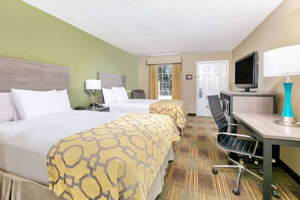 Ein Hotelzimmer mit zwei Betten, einem Schreibtisch, einem Fernseher und einem Sessel.