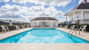 Una piscina rectangular con un indicador de profundidad de 1.5 metros, rodeada de sillas de plástico blanco y una cerca.