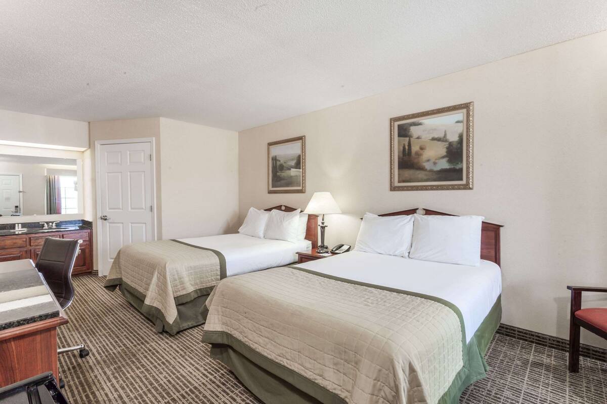A hotel room with two beds, a desk with a chair, a mirror, and two framed pictures on the wall.