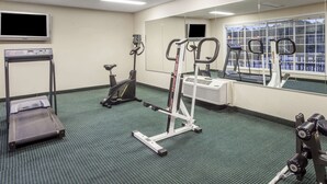 Un gimnasio con caminadora, elíptica y máquinas de pesas, un espejo grande y un televisor en la pared.