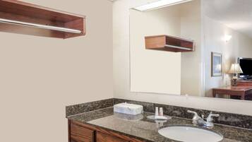 A bathroom with a granite countertop, a white sink, wooden cabinets, a mirror, and a wooden shelf above the mirror.