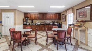 Un comedor con una mesa redonda y sillas, armarios de madera y una mesa de buffet con frutas y verduras.