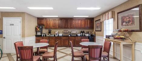 A dining area with a round table and chairs, wooden cabinets, and a buffet table with fruits and vegetables.