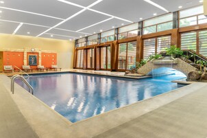 Une grande piscine intérieure dotée d’une cascade, de portes coulissantes en bois et d’un espace détente avec des fauteuils.