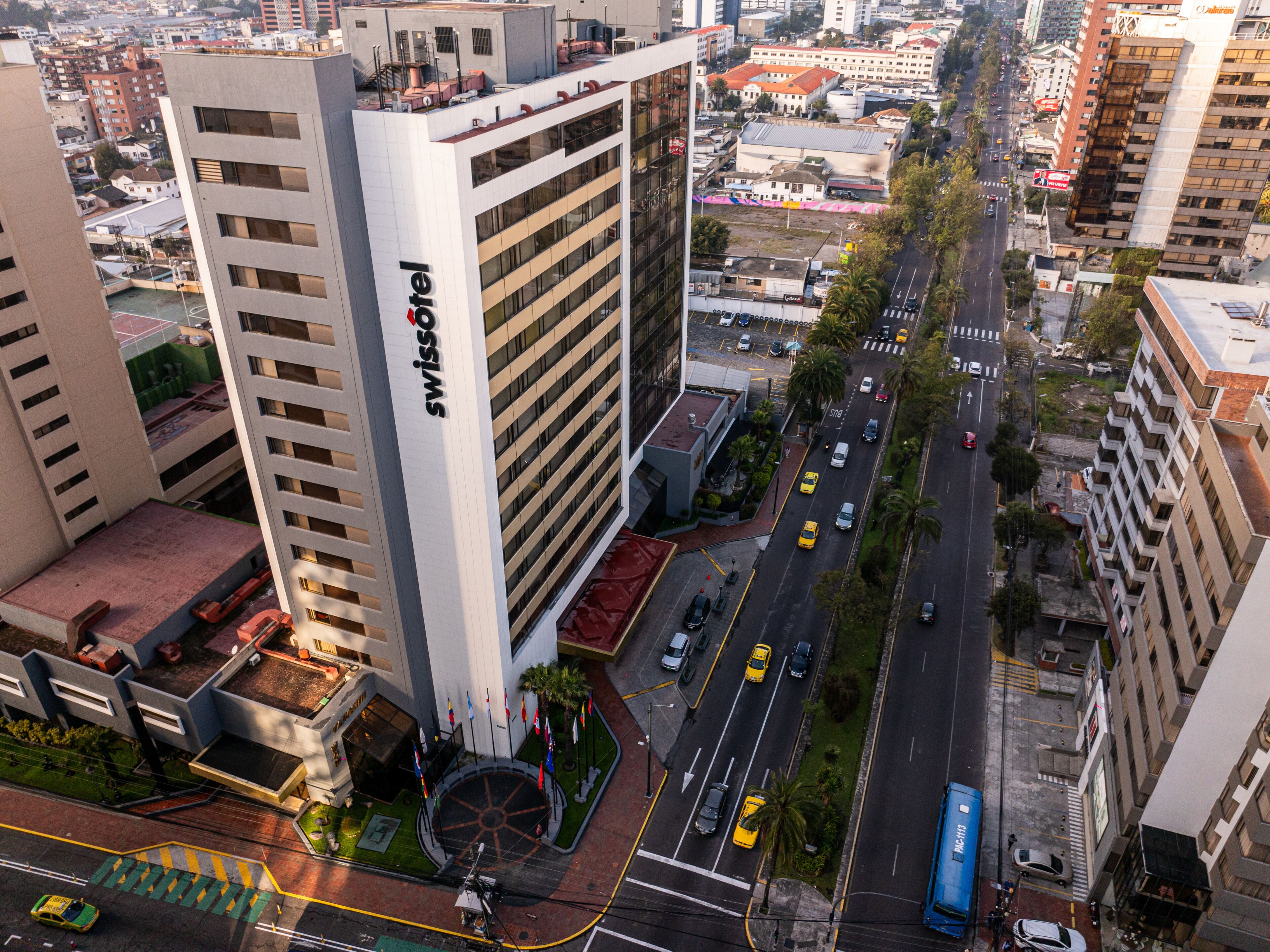 A modern hotel with a prominent sign, surrounded by a cityscape with a busy street and other buildings.