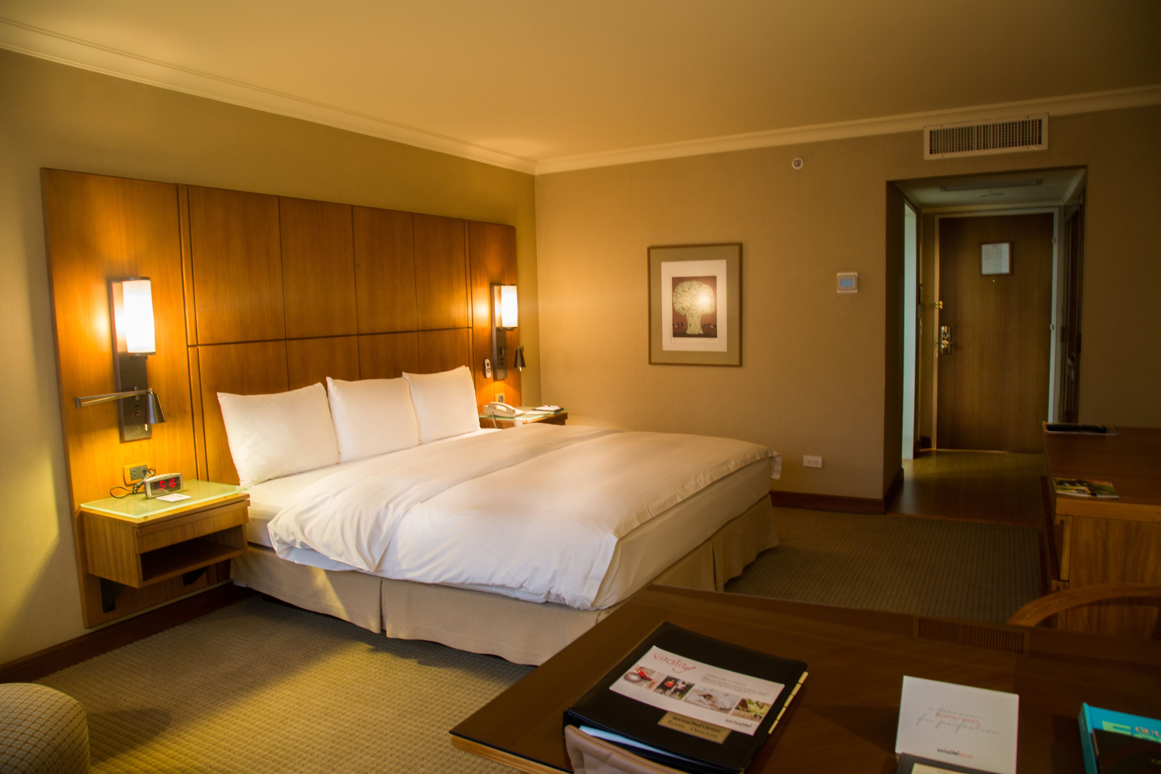A hotel room with a large bed, bedside lamps, a desk, and a framed picture on the wall.