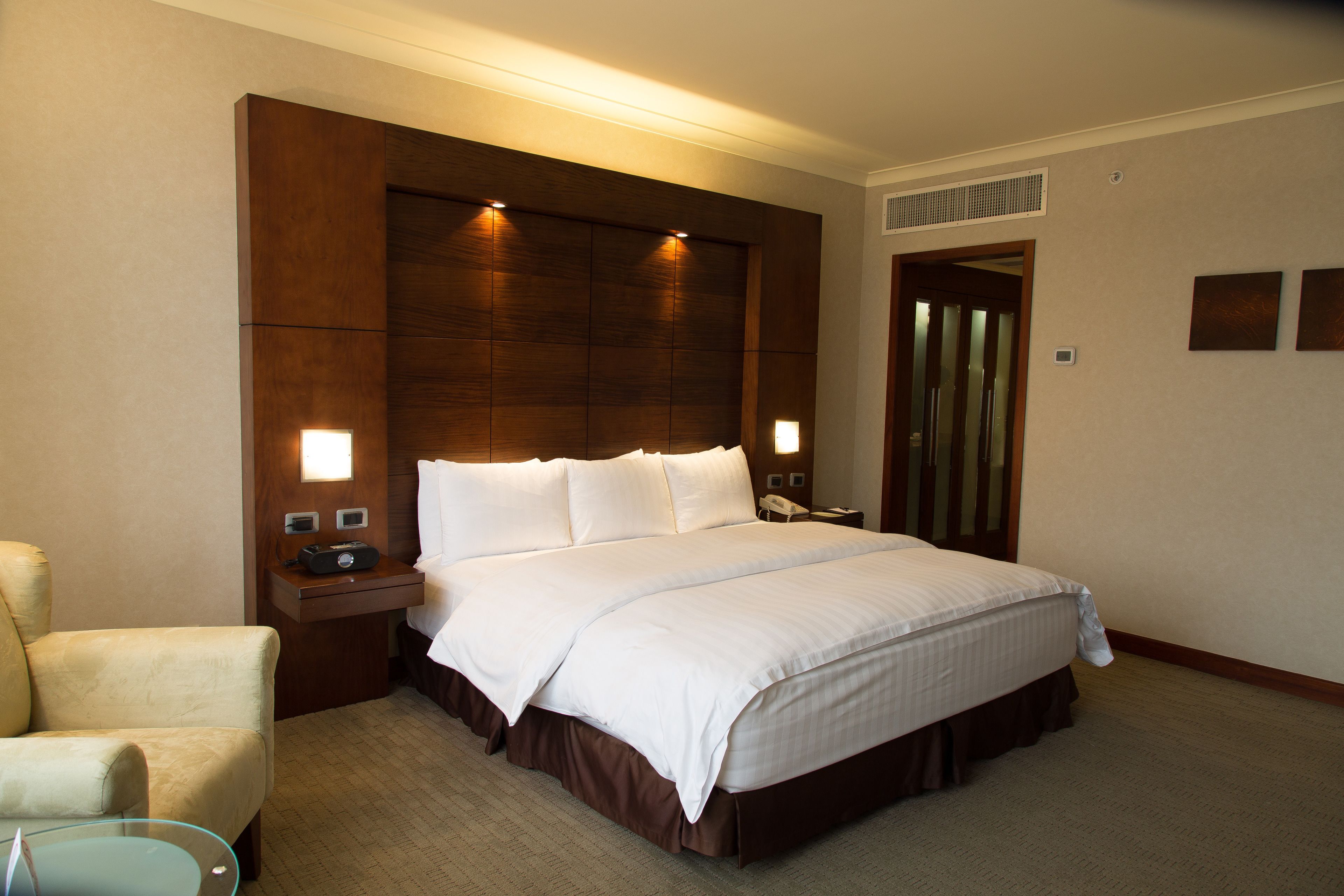 Habitación de hotel con una cama grande, una mesita de noche con lámpara, una silla y una pequeña mesa.
