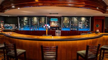 A bar area with a curved wooden counter, multiple shelves of bottles, and three bar stools.