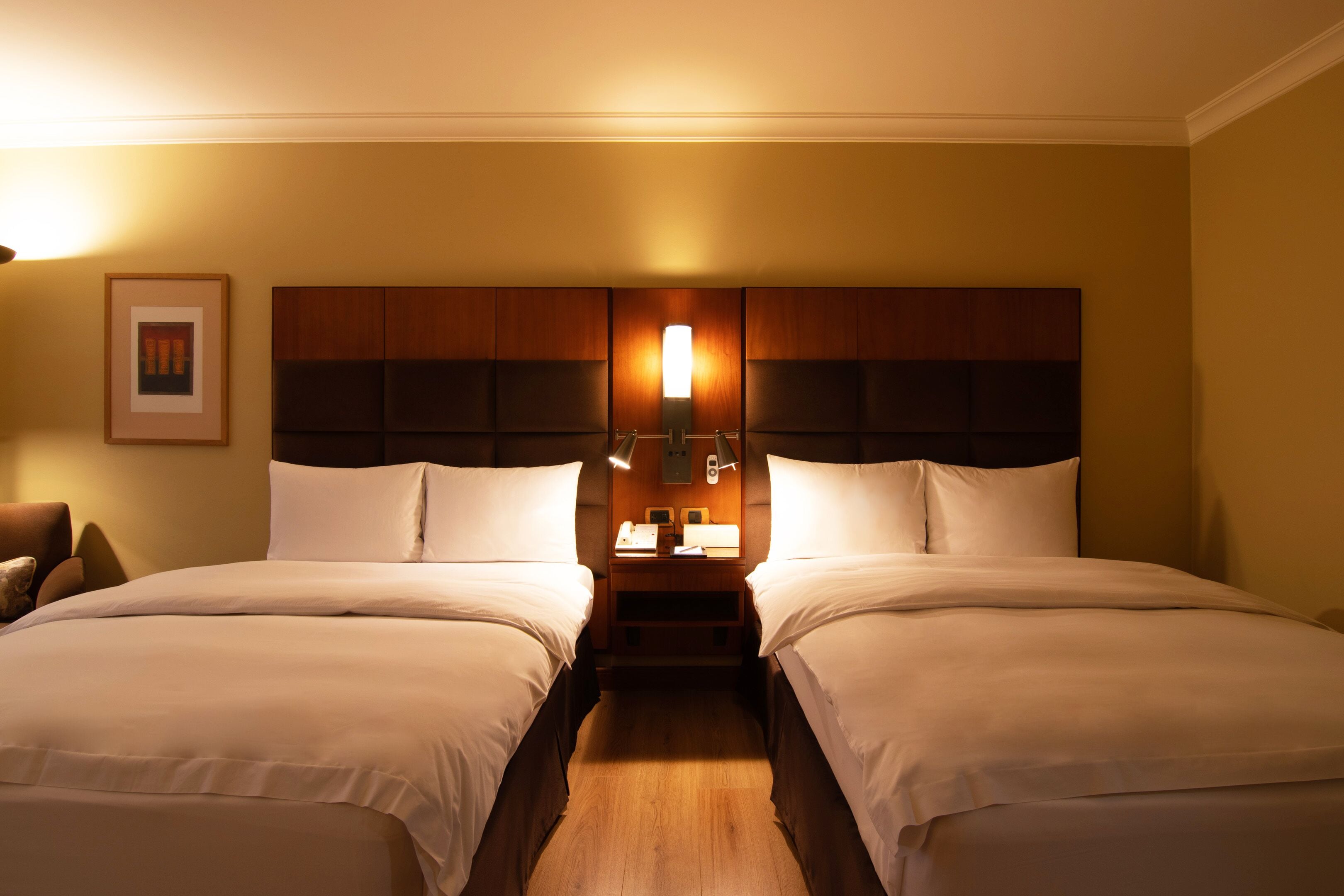 A hotel room with two beds, a wooden headboard, bedside lamps, and a framed picture on the wall.