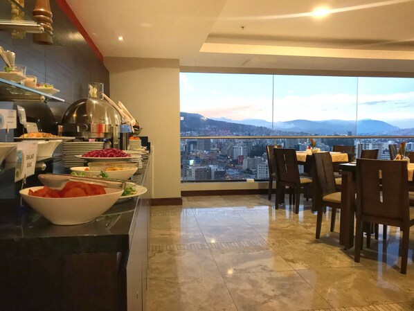 A dining area with a buffet setup and a city view. - Swissotel Quito (Quito)