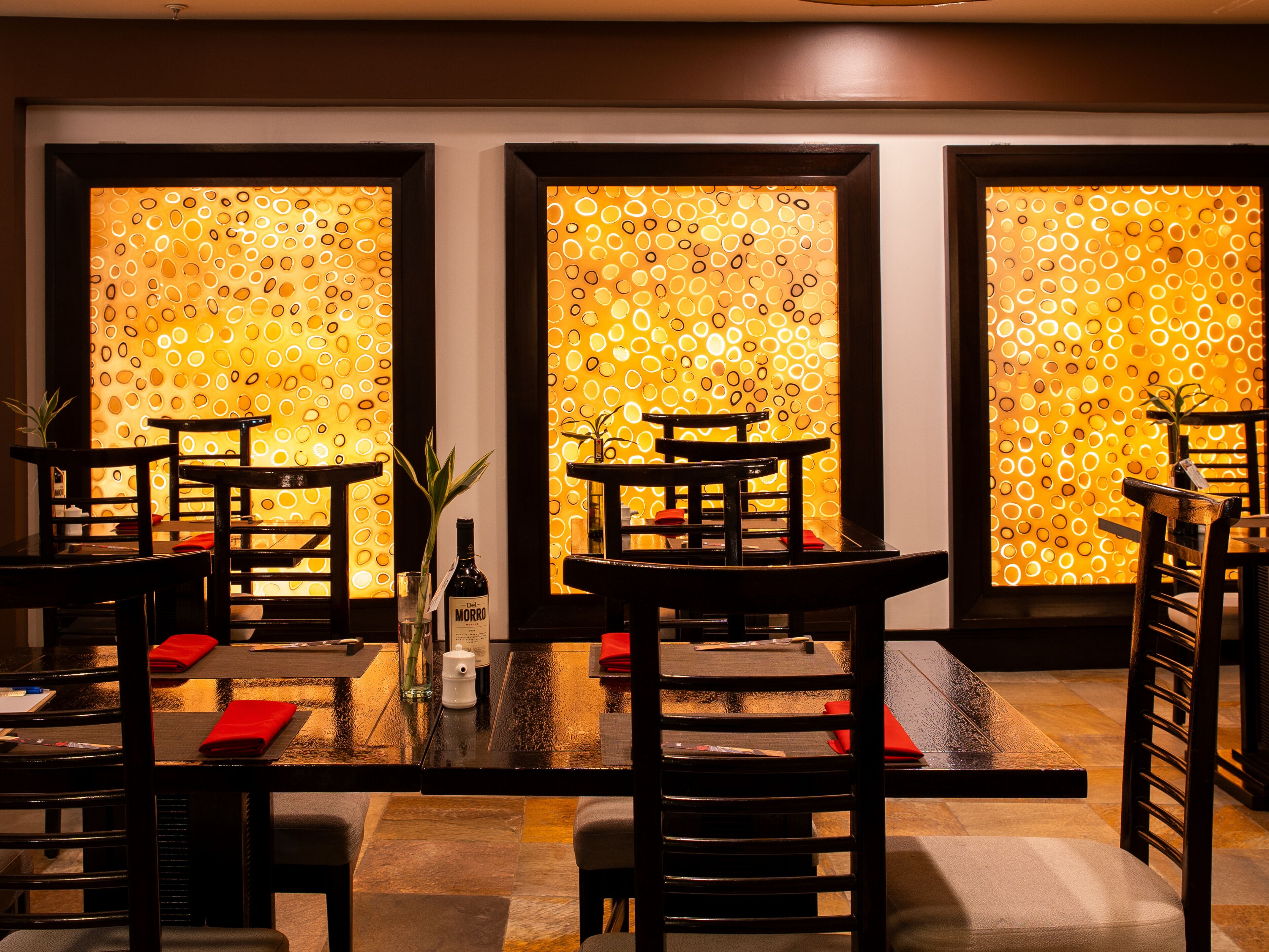 Ein Restaurantinnenraum mit Tischen und Stühlen, eine Wand mit dekorativen Kreismustern und eine Weinflasche auf dem Tisch.