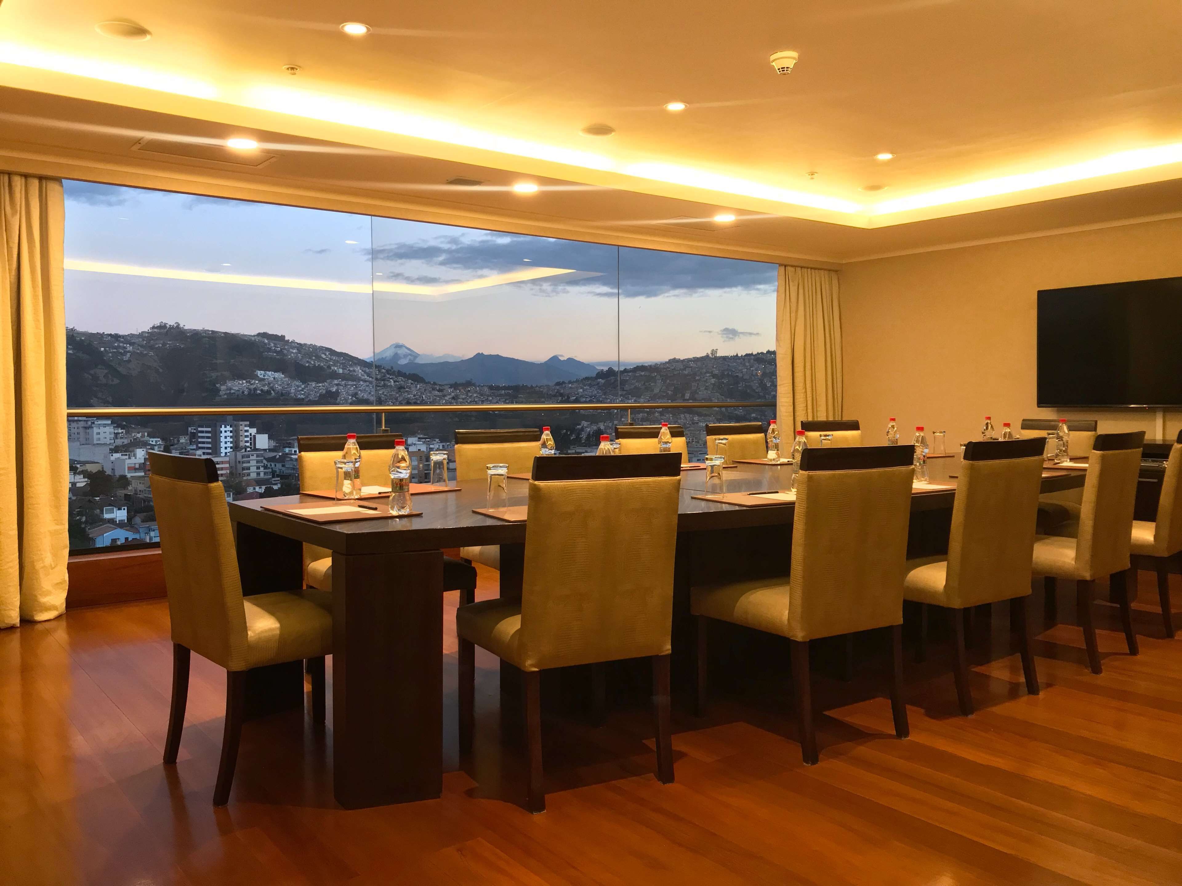 A conference room with a large table, chairs, and a view of a cityscape through a large window.