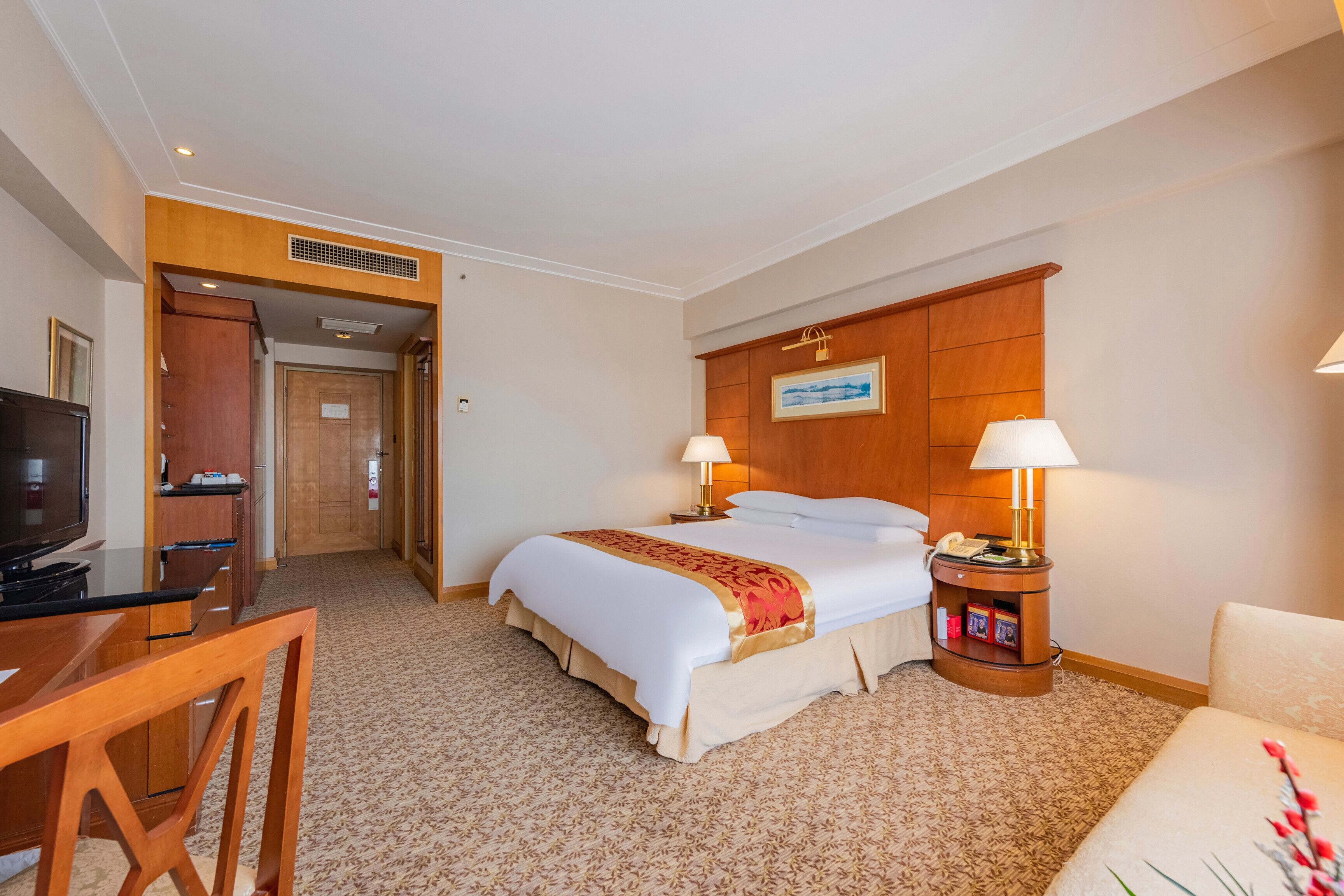 A hotel room with a bed, bedside tables, a desk, and a television.
