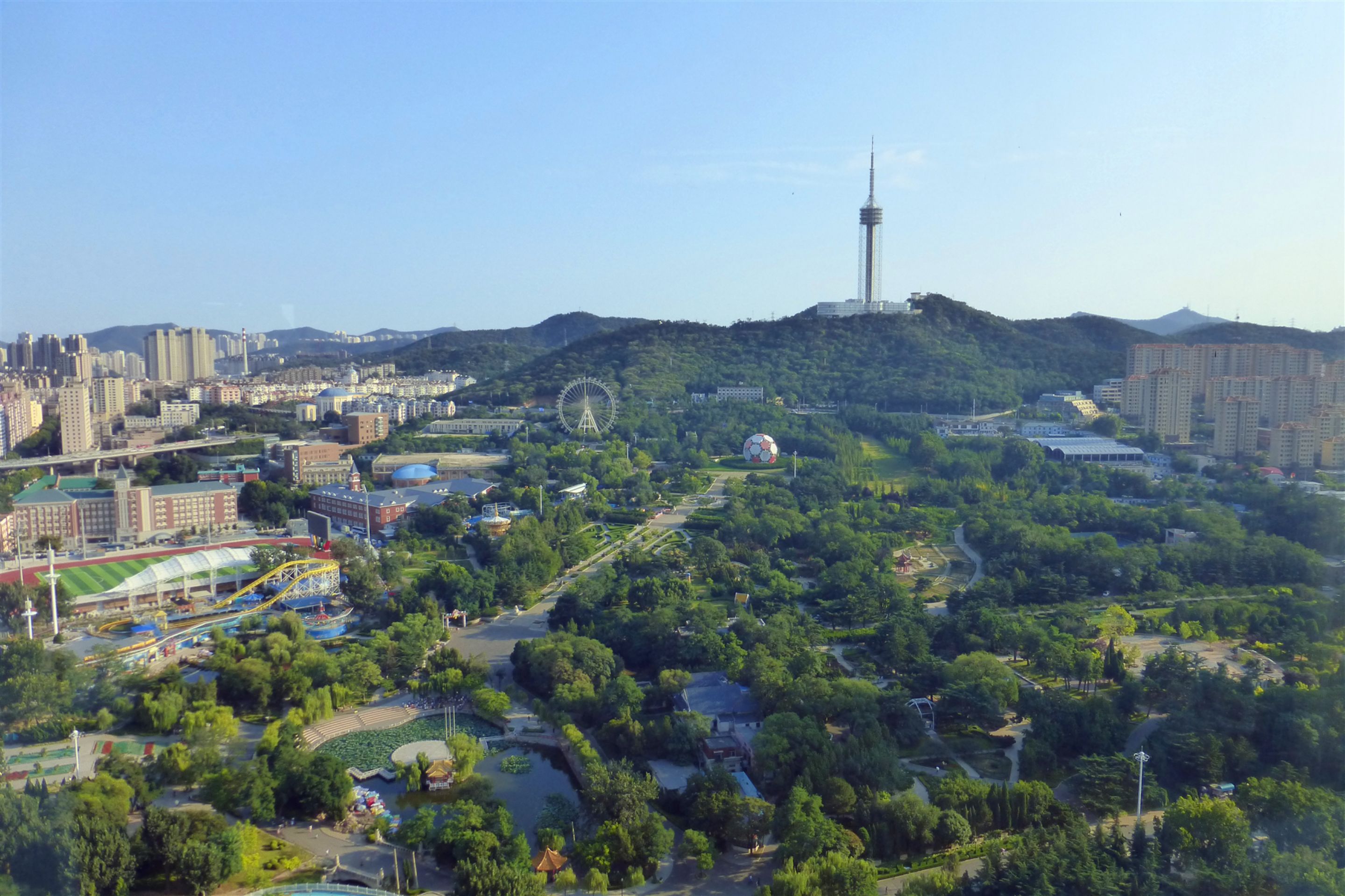A cityscape with a prominent tower, a large Ferris wheel, and a park area with pathways and greenery.