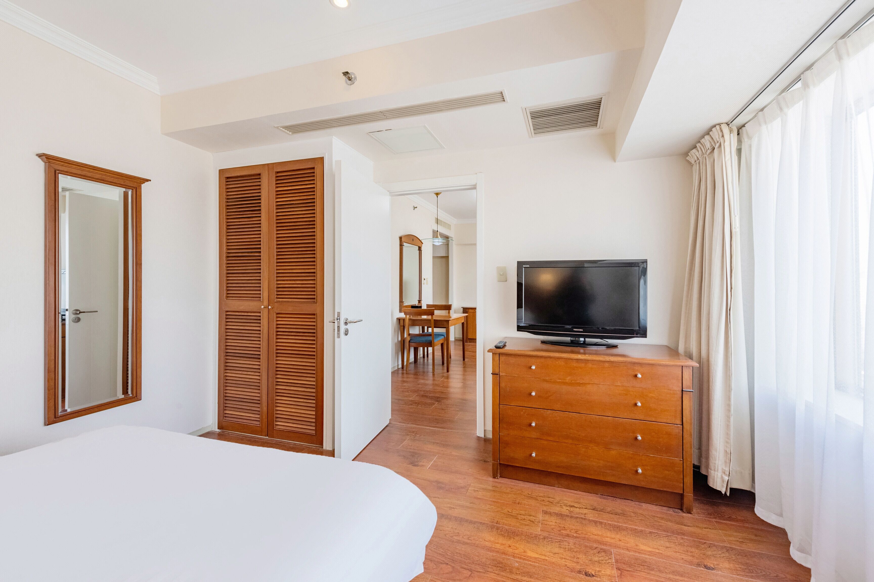 Habitación de hotel con cama, armario de madera, televisión y una zona de comedor al fondo.