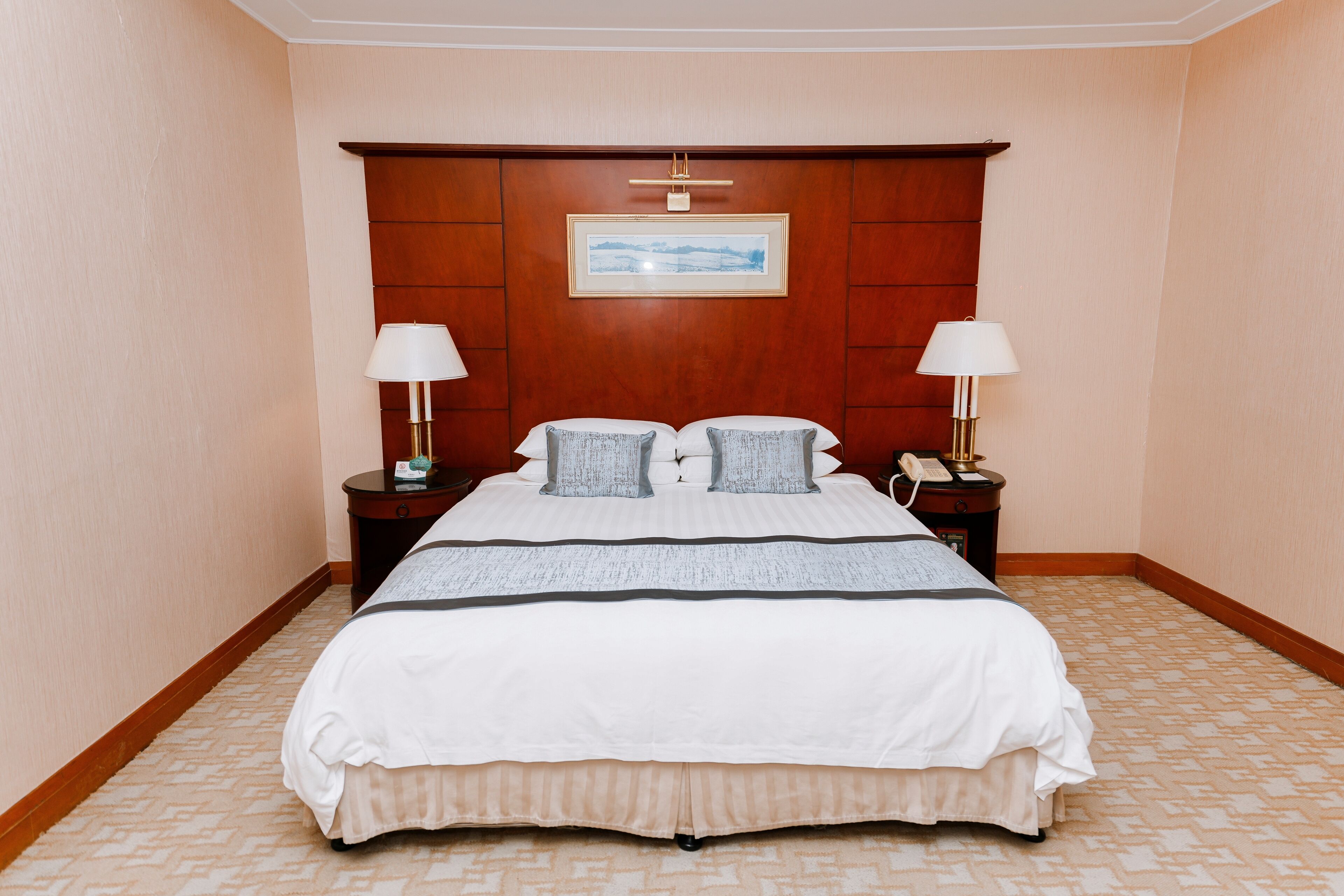 Habitación de hotel con una cama grande, dos mesitas de noche con lámparas, un cabecero de madera y un cuadro enmarcado en la pared.