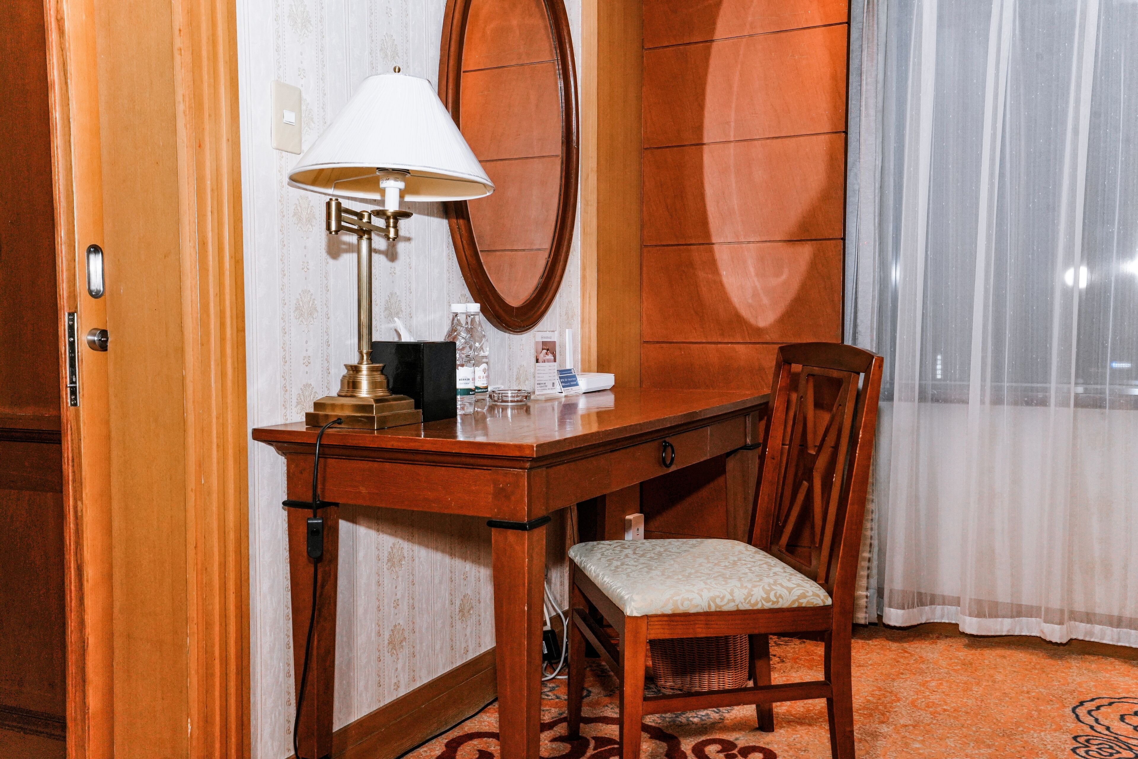 A wooden desk with a lamp, a chair, and a mirror in a hotel room.