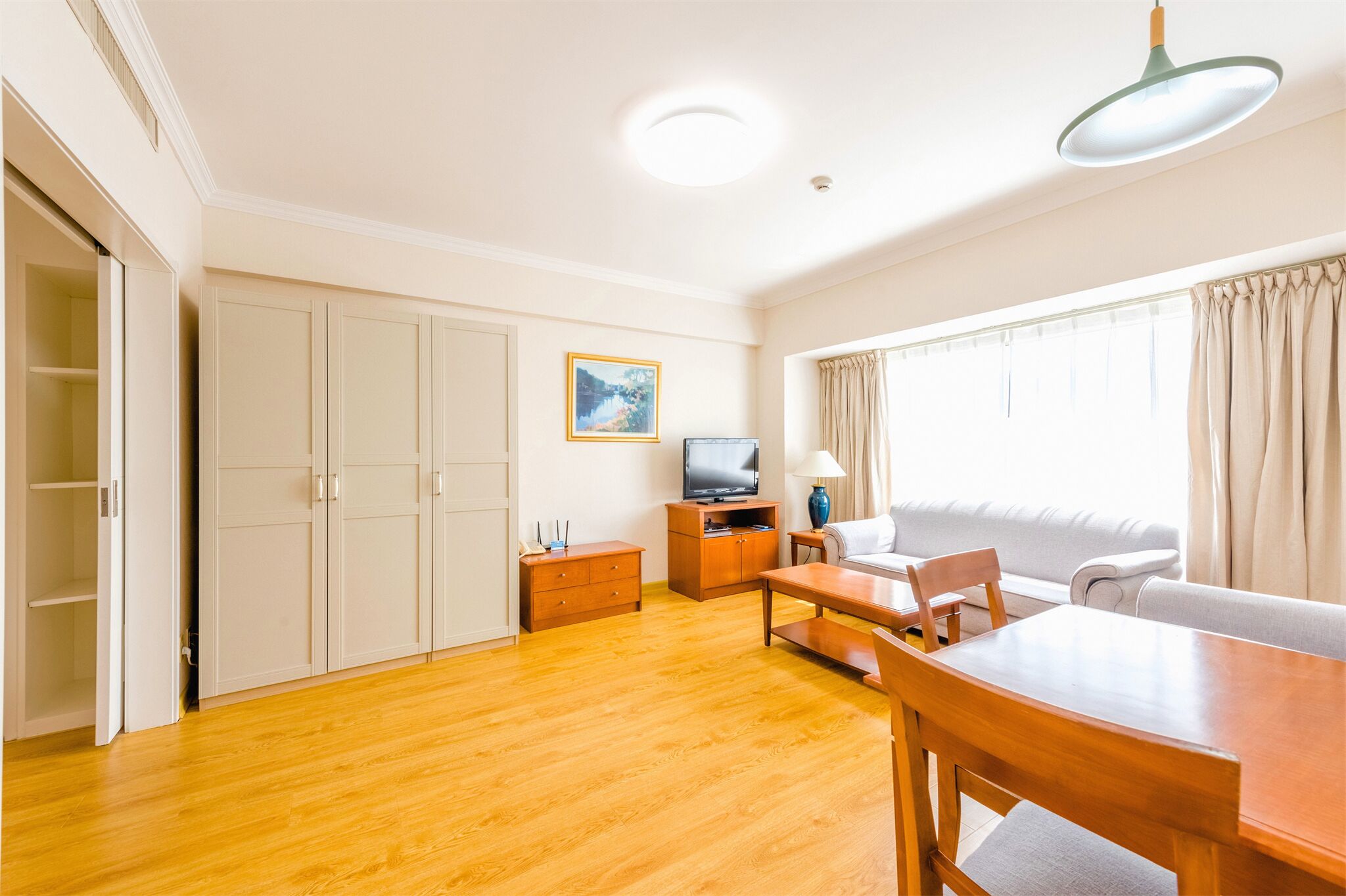 A spacious living room with a wooden floor, a sofa, a dining table, and a TV.