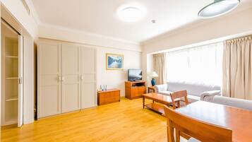 A spacious living room with a wooden floor, a sofa, a dining table, and a TV.