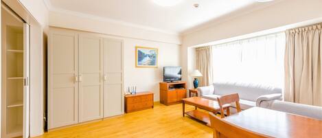 A spacious living room with a wooden floor, a sofa, a dining table, and a TV.
