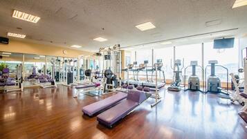 A gym with various exercise equipment, wooden flooring, and large windows.