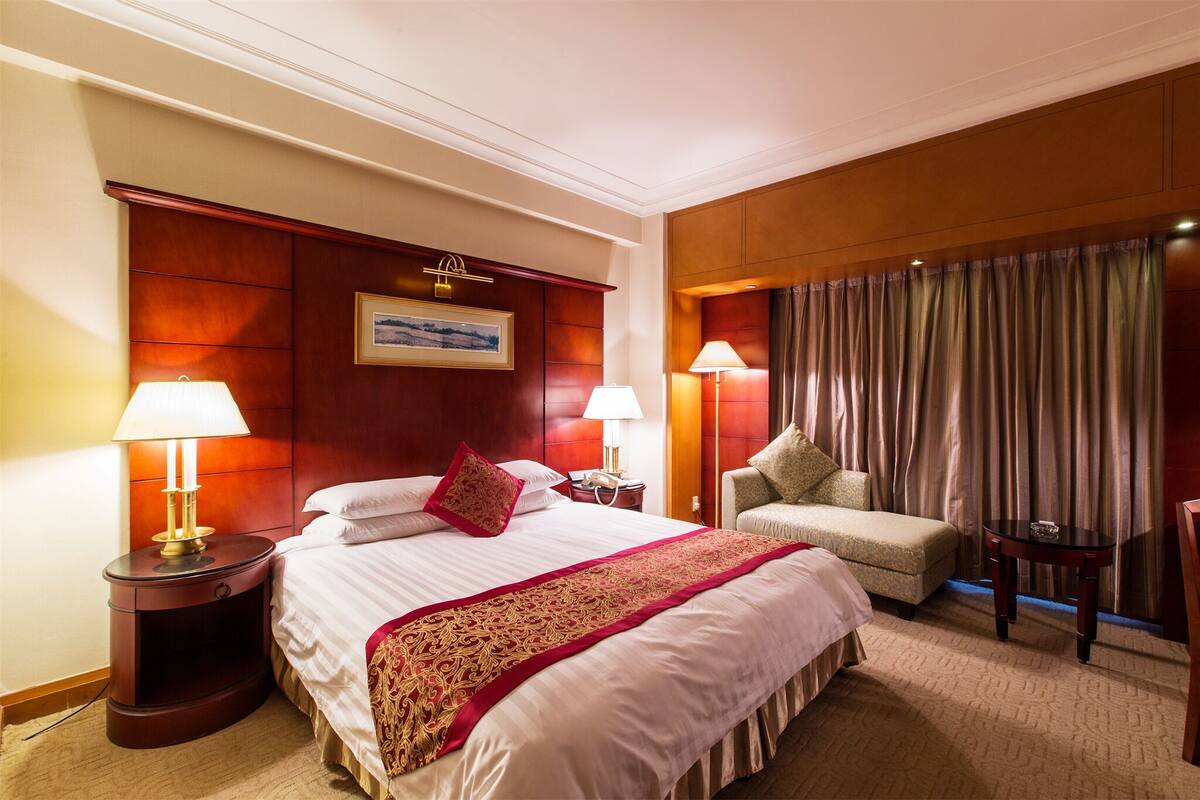 A hotel room with a large bed, two bedside tables, a chair, and a view of the city through curtains.