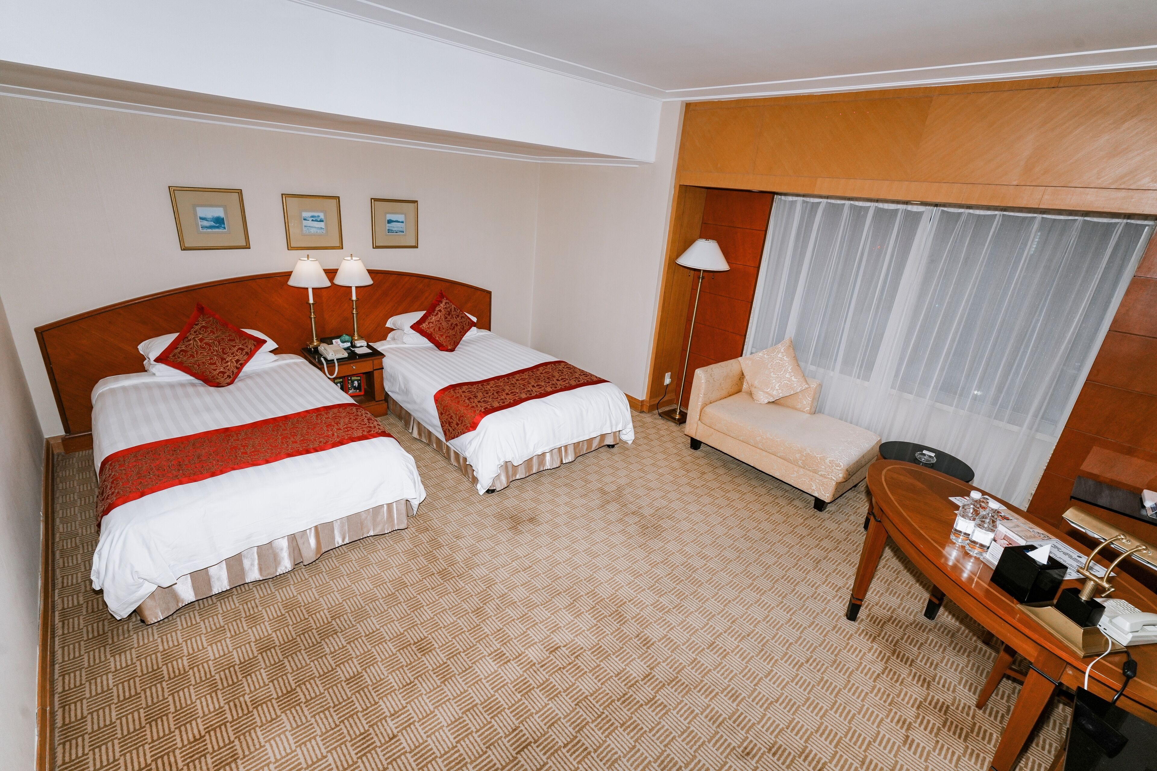 Habitación de hotel con dos camas, un sofá, un escritorio y un ventanal grande.