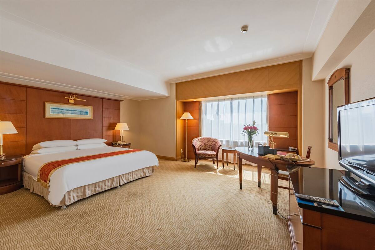 A hotel room with a large bed, a desk with a chair, a television, and a window with curtains.