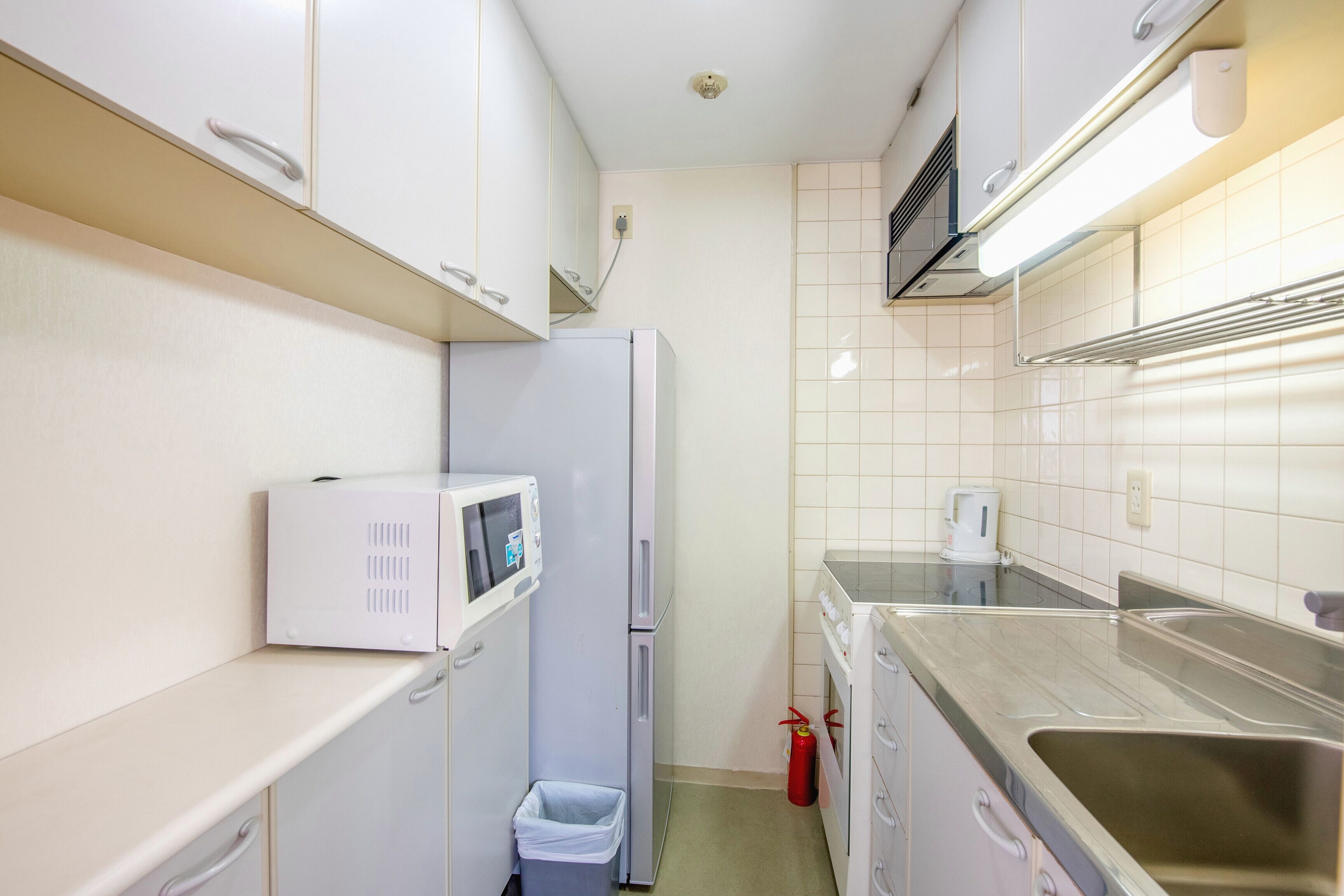 Une cuisine de taille réduite, avec des meubles blancs, un four à micro-ondes, un réfrigérateur, un évier et une cuisinière à gaz.