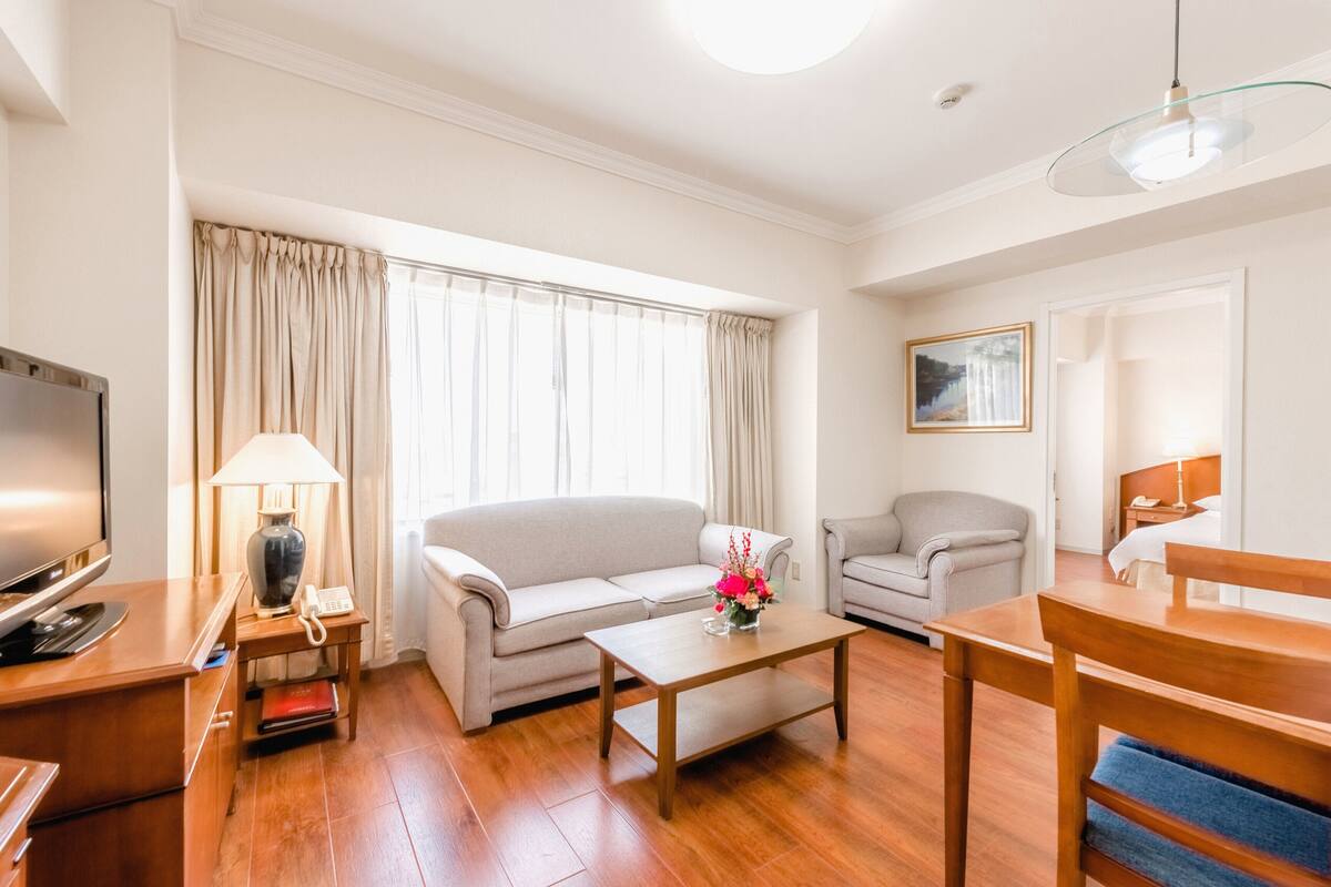 A hotel room with a sofa, a coffee table, a TV, a lamp, and a painting on the wall.