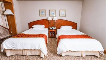 A hotel room with two beds, a nightstand with lamps, and three framed pictures on the wall.