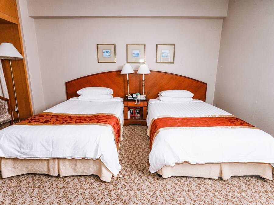 A hotel room with two beds, a nightstand with lamps, and three framed pictures on the wall.