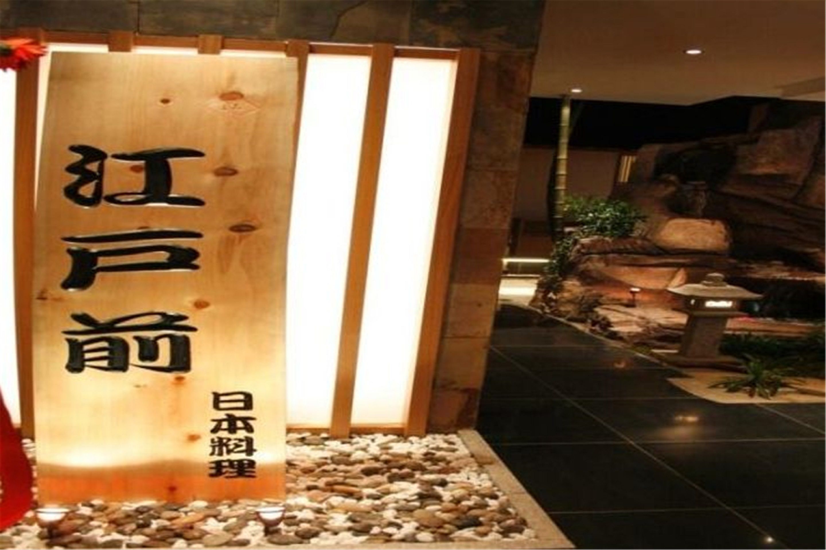 Ein hölzernes Schild mit japanischen Schriftzeichen, eine kiesbestreute Fläche und eine Felsformation im Hintergrund.