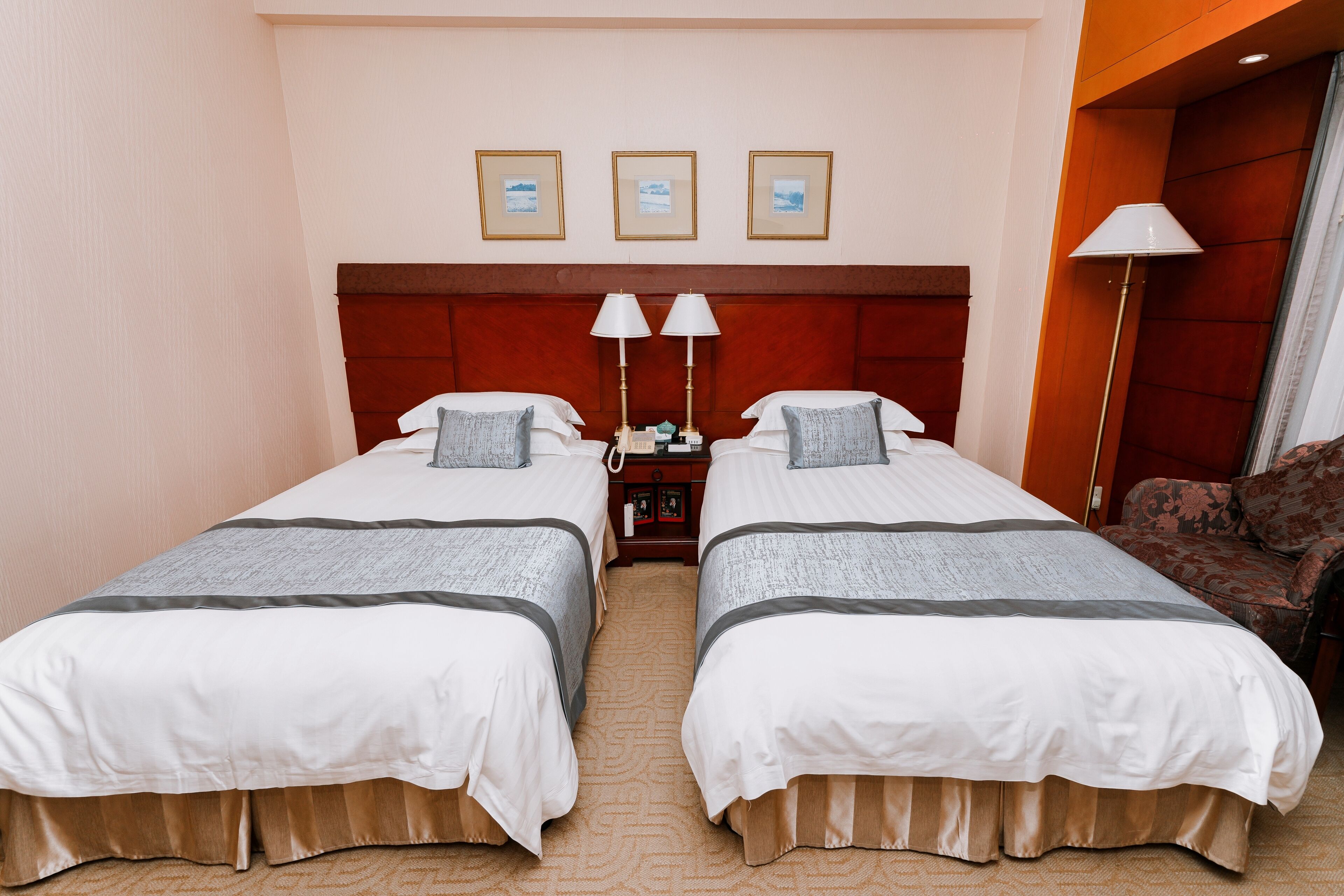 Ein Hotelzimmer mit zwei Betten, einem Nachttisch, einer Lampe und gerahmten Bildern an der Wand.