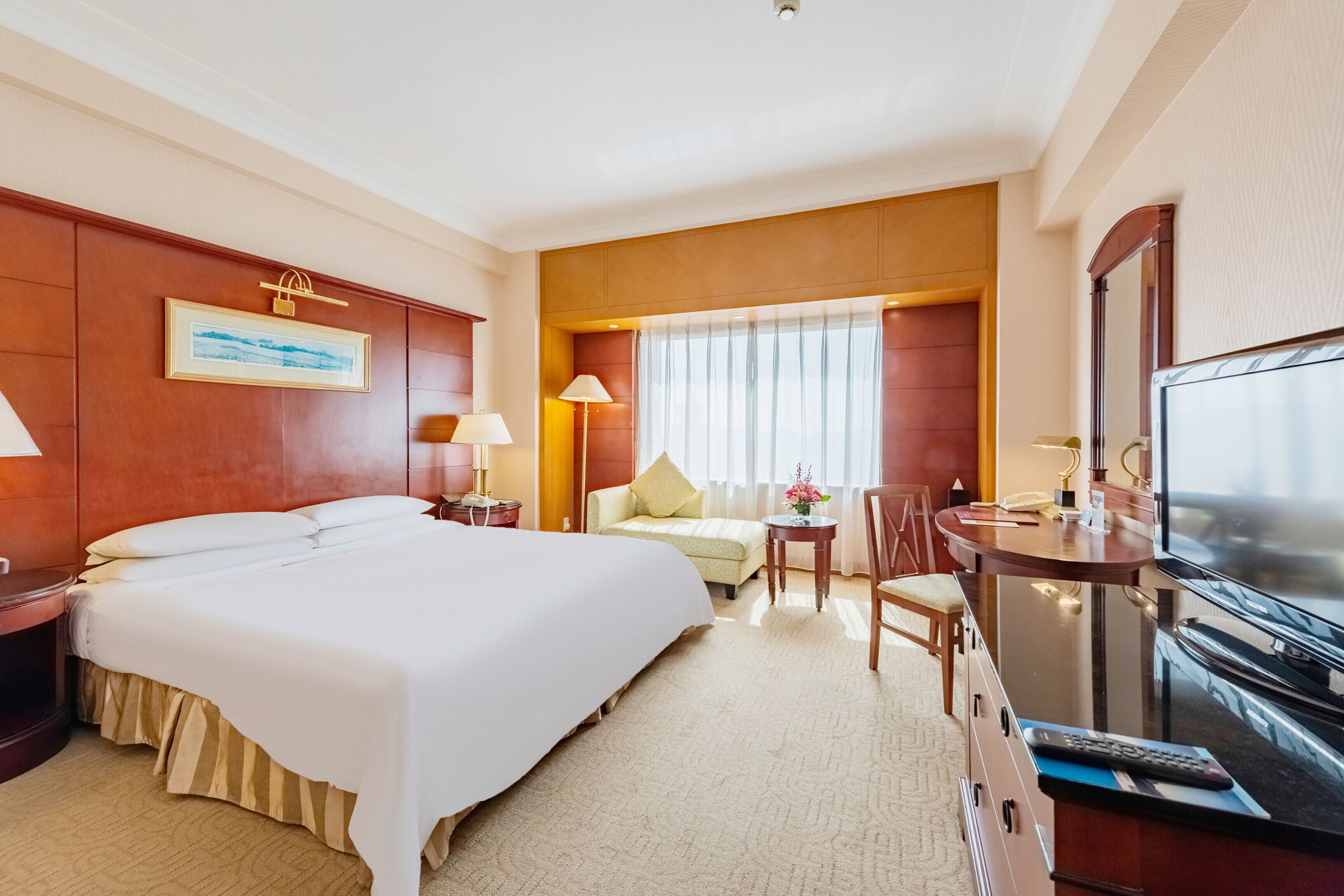 Une chambre d’hôtel avec un grand lit, un bureau avec une télévision, une chaise et une petite table avec une lampe.